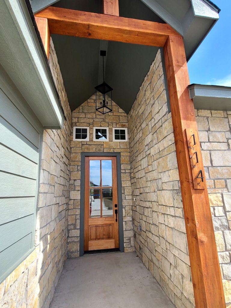 Front of home built in Tom Bean, Texas with cedar posts and stone siding. Includes modern light fixture in entryway